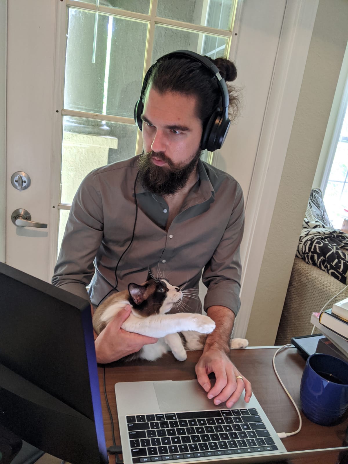 Picture of Sam Holley-Kline sitting at his laptop with headphones and his cat on his lap.